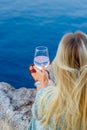 A girl sits on the seashore with glass in her hands.