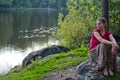 The girl sits on stone in the forest, by the lake. Quiet romantic photo