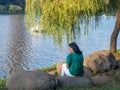 girl sits on a stone by the lake. Lonely girl. Rest in the park. Stones by the lake