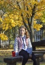 a girl sits at a table in an autumn park, headphones are on her head Royalty Free Stock Photo