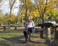 a girl sits at a table in an autumn park, headphones are on her head Royalty Free Stock Photo