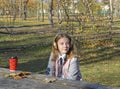 a girl sits at a table in an autumn park, headphones are on her head Royalty Free Stock Photo