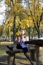 a girl sits at a table in an autumn park, headphones are on her head Royalty Free Stock Photo