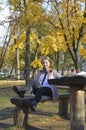 a girl sits at a table in an autumn park, headphones are on her head Royalty Free Stock Photo