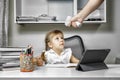 Girl sits at a table with a tablet and writes in a notebook. hand with an electronic thermometer aimed at the child Royalty Free Stock Photo