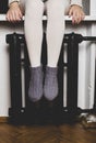 The girl sits on the windowsill and heats her legs in knitted woolen socks at the radiator, on a cold winter evening Royalty Free Stock Photo