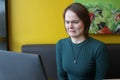 A girl sits, works at a laptop at a table in a cafe on a brown sofa against a yellow wall. On the face is an expression Royalty Free Stock Photo