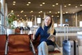 Girl sitting in airport waiting room with valise, using tablet and showing thumbs up. Royalty Free Stock Photo