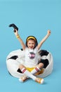 Girl sitting on bean bag chair, raising hands up while celebrating winning Royalty Free Stock Photo