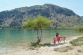A girl is sitting on a bench near a tree on lake kurnas. Island of Crete. Royalty Free Stock Photo
