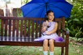 Girl sitting with blue umbrella on wooden bench Royalty Free Stock Photo
