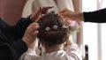 The girl is sitting on a chair and stylists fix her hair.