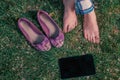 Girl sitting crosslegged on grass with her shoes and tablet computer near, top view