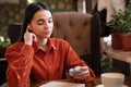 Girl sitting with earphone in ear holding charging case for wireless headphones while relaxing in cafe Royalty Free Stock Photo