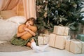 Girl sitting on the floor by the bed and the Christmas tree hugging a pillow Royalty Free Stock Photo