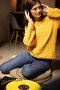 girl sitting on floor enjoys to music with headphones and analog turntable