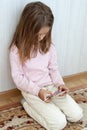 girl is sitting on the floor and playing mobile games on her phone. Concept of using mobile phone by children for games and video Royalty Free Stock Photo