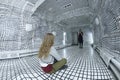 Girl sitting on the floor of the white grid acoustic room, another one taking picture of her