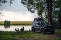 The girl is sitting on a folding chair. Picnic. off-road vehicle on the shore of the lake, forest in the middle of wilderness. Royalty Free Stock Photo