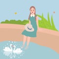 Girl sitting with foot in water looking at two swan swimming in lake