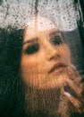 A girl is sitting in front of a window, the weather is rainy. Raindrops are visible on the window