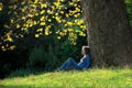 Girl sitting on the grass under maple tree in autumn Royalty Free Stock Photo