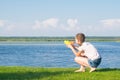 The girl is sitting on the green grass and playing with a water pistol, against the blue sky and the lake, there is a place for an Royalty Free Stock Photo