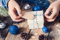 Girl sitting at her desk tying gift tag for Christmas present. Closeup of hands and white box with blue bow on dark wooden Royalty Free Stock Photo