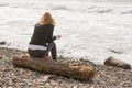 Girl sitting on log on the coast and looks at sea Royalty Free Stock Photo