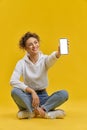 Girl sitting in lotos pose, showing smartphone.