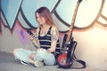 Girl sitting near graffiti wall with a guitar listening music. Royalty Free Stock Photo