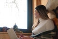 A Girl Sitting Next To The Window Looking Outside During The Daytime- Using Her Laptop Royalty Free Stock Photo