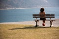 A girl sitting over her shoulder on a wooden bench looks at a mountain lake. Royalty Free Stock Photo