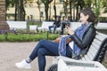 Girl sitting on a Park bench in white headphones looking at phone and smiling, Russia, St. Petersburg, September, 2018