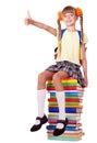 Girl sitting on pile of books showing thumb up.