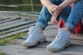 Girl sitting on a river beach on a wooden pier. Closeup of teenage legs in modern and trendy white sneakers and rolled up jeans. Royalty Free Stock Photo