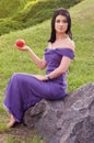 Girl sitting on rock and holds apple in his hand.