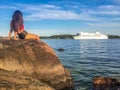 Girl sitting on rock by shore watching passing ship