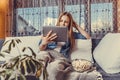 Girl sitting on the sofa covered with a blanket and watching movie on tablet Royalty Free Stock Photo