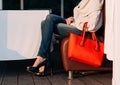 Girl sitting on the sofa of summer cafe with a big red super fashionable handbags in a sweater jeans and sneakers on a warm summer