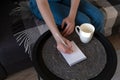 Girl sitting on sofa and writes notes. Cup of water on coffee table, indoors. Concept studying