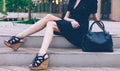 Girl sitting on the stairs with a big black super fashionable handbags in a dress and High Wedge Sandals on a warm summer evening Royalty Free Stock Photo