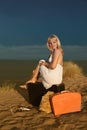 Girl sitting on a suitcase at the beach