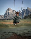 Girl sitting on swing on meadows at Alpe di Siusi during summer with view to mountains of Plattkofel and Langkofel in the Dolomite Royalty Free Stock Photo