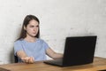 The girl sitting at the table, looks indignantly at the laptop screen Royalty Free Stock Photo