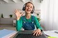 Girl sitting at table, using laptop, waving to webcam Royalty Free Stock Photo