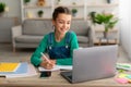 Girl sitting at table, using laptop, writing in notebook Royalty Free Stock Photo