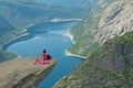 Girl sitting on Trolltunga rock with Norwegian flag, Norway. Mountain lake Ringedalsvatnet landscape Royalty Free Stock Photo