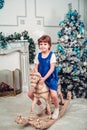 the girl is sitting on a wooden horse near a Christmas tree