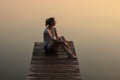 Girl sitting on a wooden pier or jetty on the lake at sunset Royalty Free Stock Photo